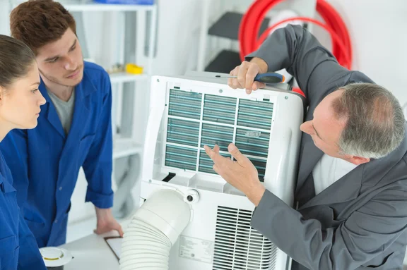 Ein Lehrer erklärt zwei Auszubildenden die Technik eines Klimakompressors.