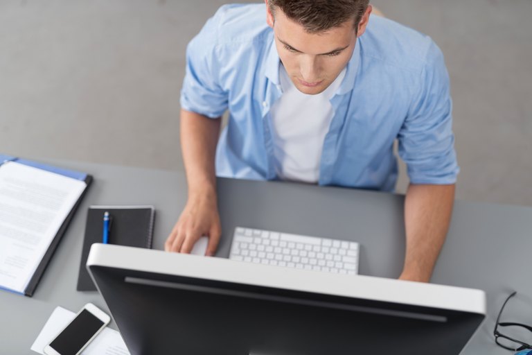 Junger Mann sitzt am Schreibtisch und arbeitet am Computer.