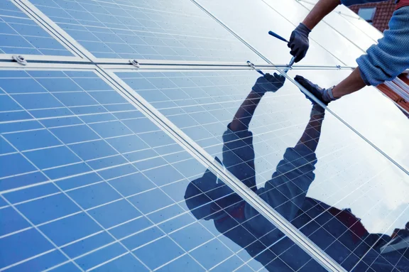 Ein Handwerker installiert eine Solaranlage auf einem Hausdach.