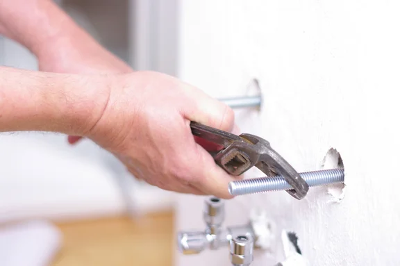 Ein Installateur arbeitet mit der Rohrzange am Wandanschluss im Bad.