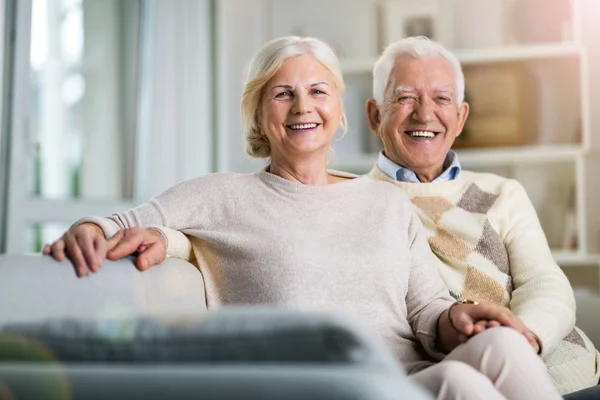  Glückliches älteres Ehepaar sitzt zu Hause auf dem Sofa.