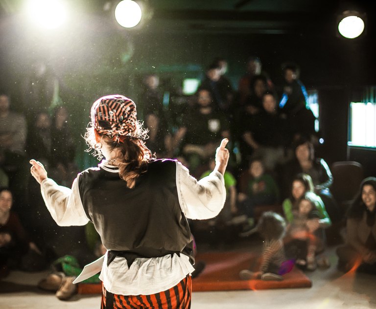 Ein Entertainer der darstellenden Künste ist von hinten im selektiven Fokus zu sehen, verkleidet als Pirat auf der Bühne während einer Komödie mit verschwommenem Publikum im Hintergrund.