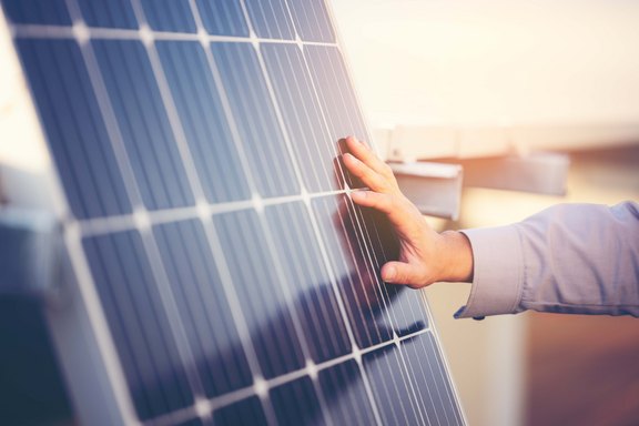 Nahaufnahme einer Hand vor Photovoltaik-Solarzellen beim Sonnenuntergang