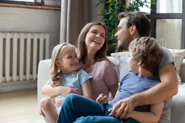 Glückliche Eltern mit kleinem Sohn und Tochter, die auf dem Boden im Wohnzimmer sitzen.