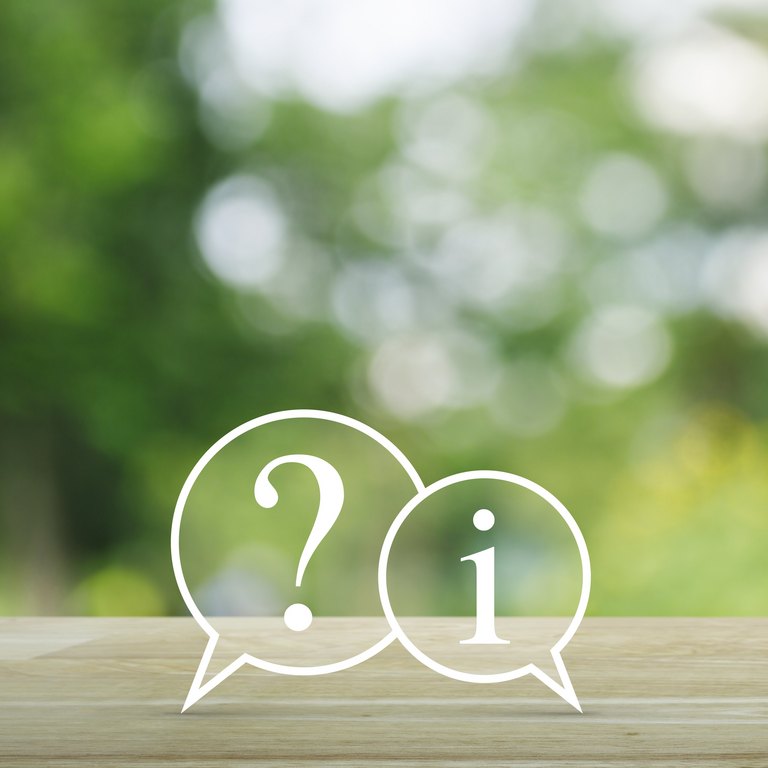 Fragezeichen und Informations-Chat-Symbol auf Holztisch über unscharfem grünen Baumhintergrund, Kundensupport-Konzept