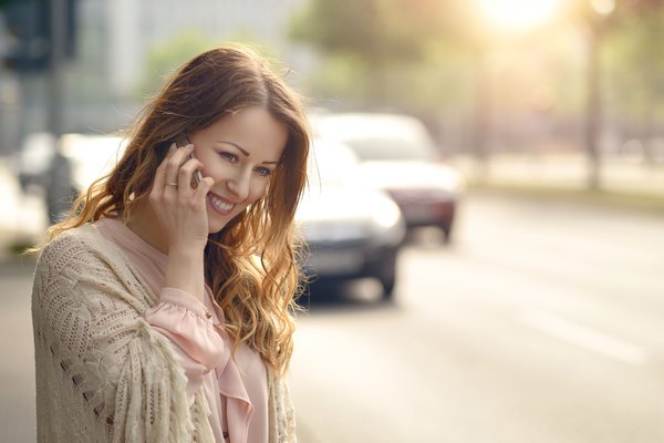 Eine junge lächelnde Frau steht an der Straße und spricht auf ihrem Handy.