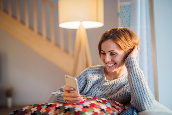 Eine glückliche junge Frau, die abends zu Hause auf einem Sofa sitzt und Smartphone verwendet